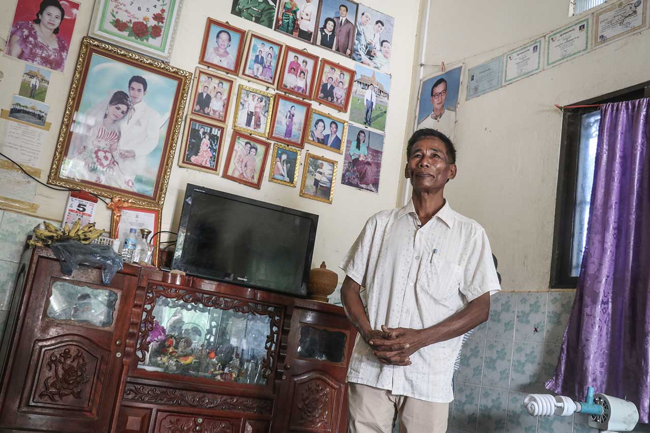 Chao La standing in a room with walls of framed photos hanging behind him.